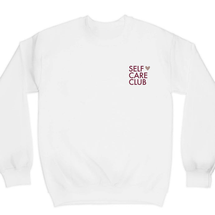 Graphic crewneck sweatshirt with the words self care club in maroon and a rose gold shimmer heart on a white sweatshirt